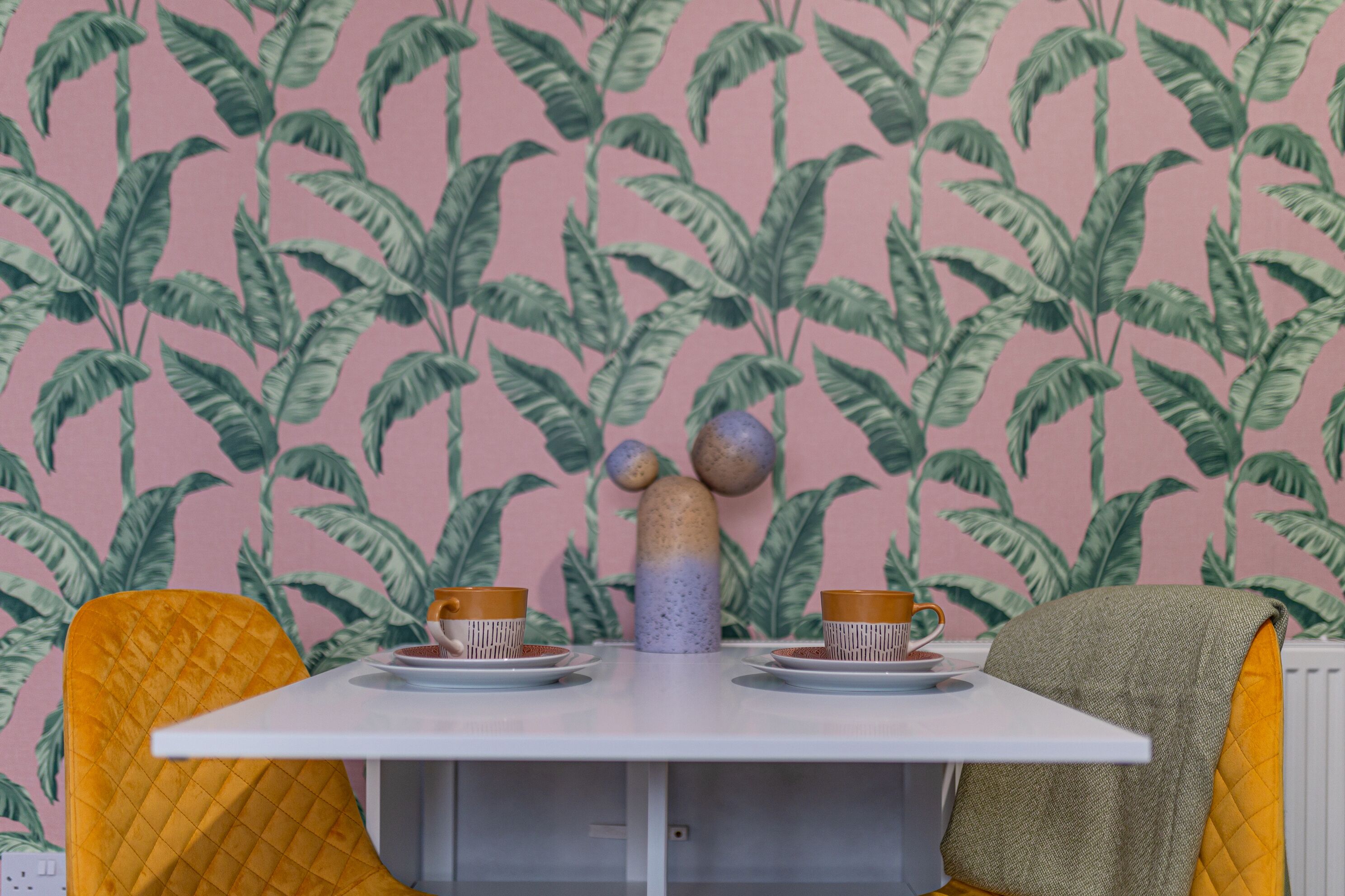Une pièce avec une table dressée pour deux personnes, un papier peint à motifs et un vase décoratif.