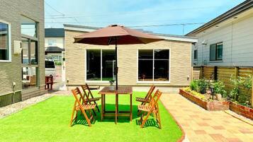 A patio with a table and chairs, a brown umbrella, and a well-maintained lawn.