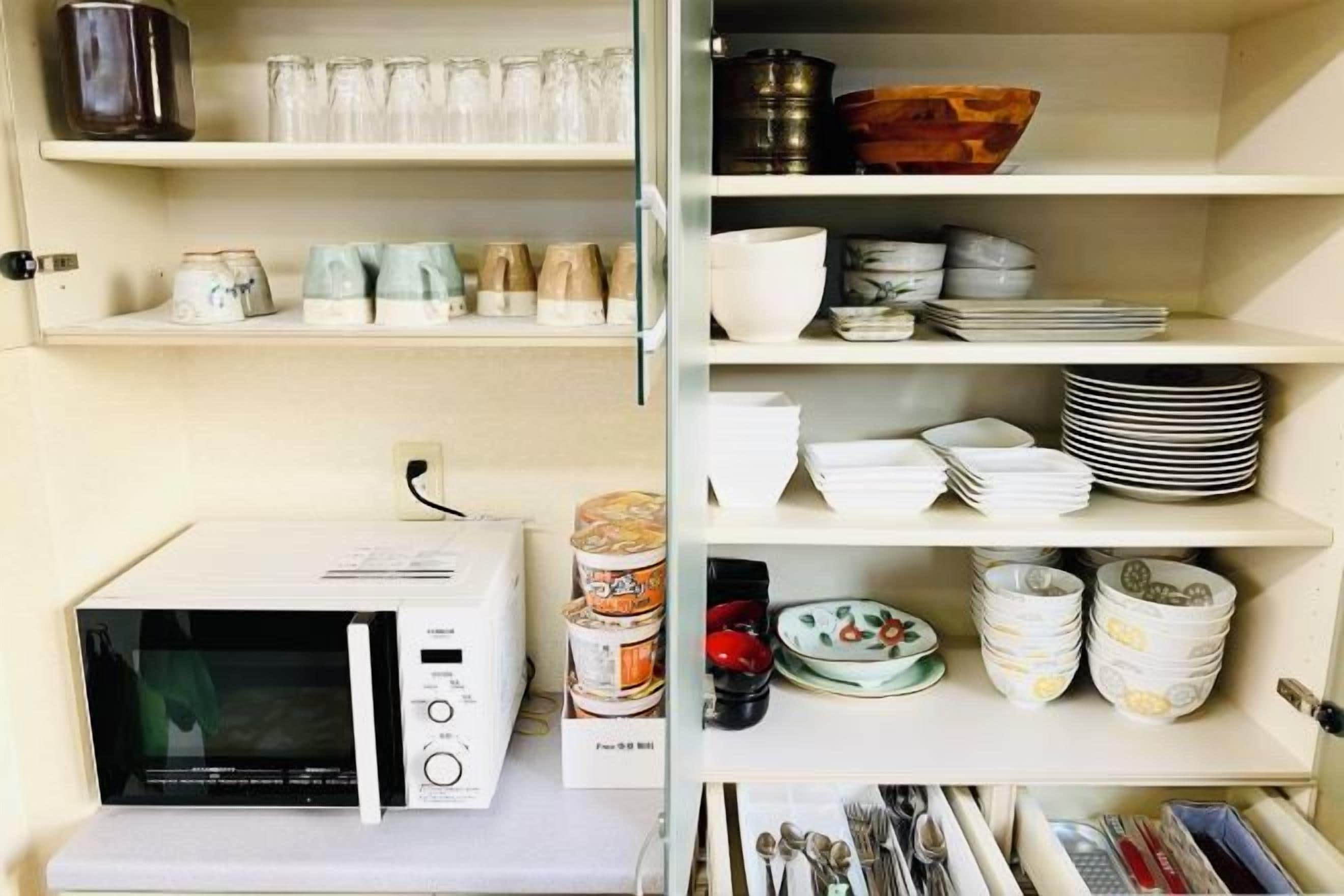 A kitchen with a microwave, shelves with dishes, and a canister.