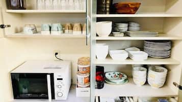 A kitchen with a microwave, shelves with dishes, and a canister.