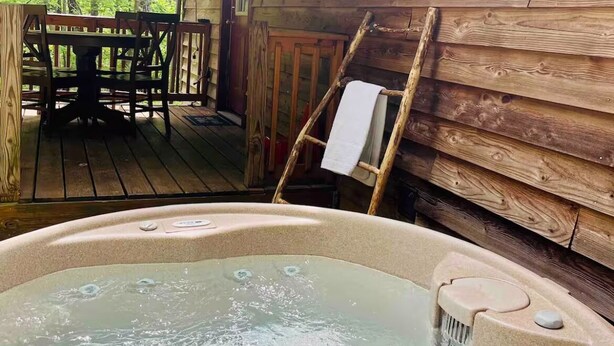 Une cabane en bois avec un jacuzzi, une table à manger et des chaises à l’extérieur.