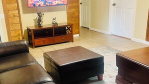 Un salon avec un canapé en cuir, une table basse en bois et un téléviseur diffusant une image de cheminée.