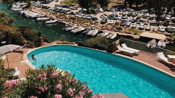 A swimming pool with a view of a parking area and surrounding greenery.