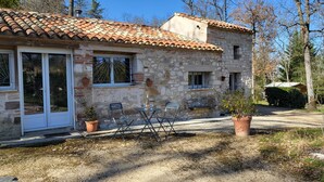 A stone building with a tiled roof, a glass door, and a small patio with two chairs and a table. - Cottage rental Gaillac countryside (Técou)