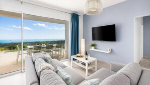 A modern living room with a large sofa, a coffee table, a flat-screen TV, and a balcony with a view. - The View - Four Bedroom Villa, Sleeps 8 (Tías)