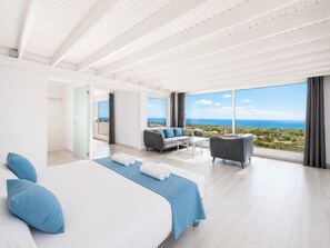 Een moderne hotelkamer met een groot bed, een bank, een bijzettafeltje en een balkon met uitzicht op zee.