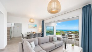 A modern living room with a large sofa, dining table, and a balcony with a view of the ocean. - The View - Four Bedroom Villa, Sleeps 8 (Tías)