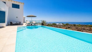 A clear blue swimming pool with lounge chairs and an umbrella, a white building, and a view of the ocean. - The View - Four Bedroom Villa, Sleeps 8 (Tías)