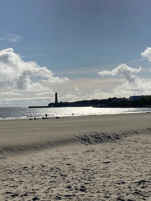 A beach with a lighthouse in the background, sandy shore, and clear sky.
