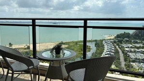 A balcony with wicker chairs and a glass table overlooking a beach and residential area. - Seaview 2B2R 6pax Condo Forest City C5-2404 (Gelang Patah)