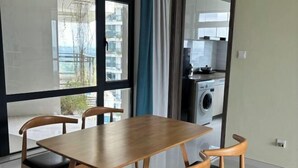 A dining area with a wooden table and chairs, a view of a laundry room, and large windows. - Seaview 2B2R 6pax Condo Forest City C5-2404 (Gelang Patah)