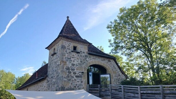 A stone building with a conical roof and a wooden fence.
