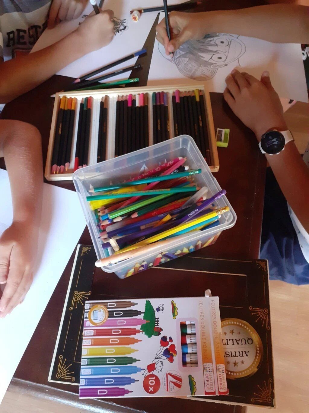 A table with various art supplies, including colored pencils, markers, and a box of crayons.