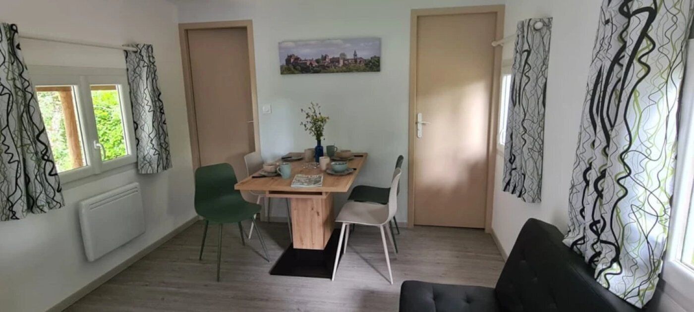 A dining area with a wooden table, chairs, and a vase of flowers. There are two doors and a window with curtains.