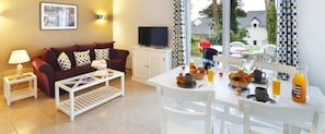 Een woonkamer met een bank, salontafel, televisie en een ontbijt gedekte eettafel.