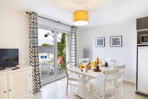 Une cuisine moderne avec un coin repas, un téléviseur et une porte-fenêtre coulissante donnant sur un espace extérieur.