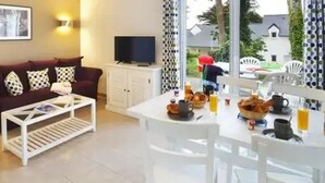 A living room with a sofa, coffee table, TV, and a dining area with a table set for breakfast.