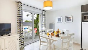 A modern kitchen with a dining area, a TV, and a large window with curtains.