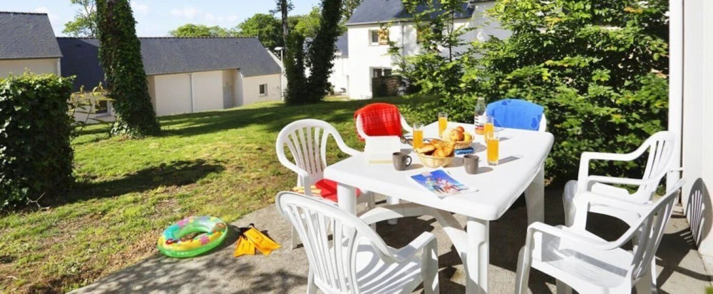 Eine Terrasse im Freien mit einem weißen Tisch und Stühlen, einem Brotkorb und einer Saftflasche.