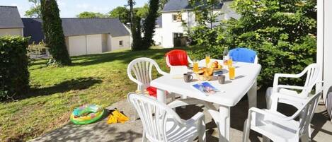 Eine Terrasse im Freien mit einem weißen Tisch und Stühlen, einem Brotkorb und einer Saftflasche.