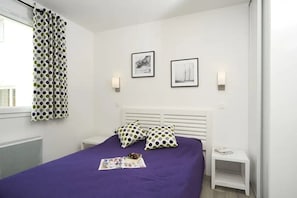 A bedroom with a purple bedspread, white headboard, and two bedside tables with lamps.