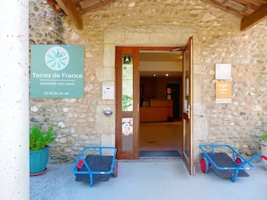 A stone building entrance with a sign for 'Terres de France Domaine des Vans,' a reception desk, and two blue carts.