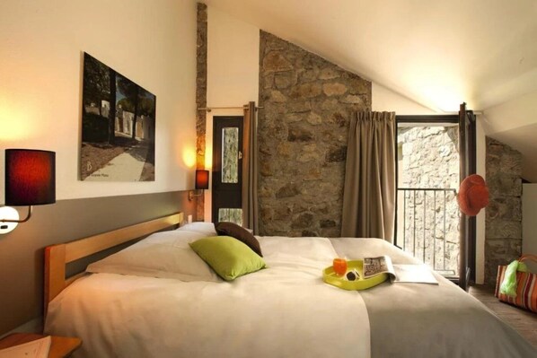Habitación de hotel con una cama grande, pared de piedra, ventana con cortinas y un cuadro en la pared.