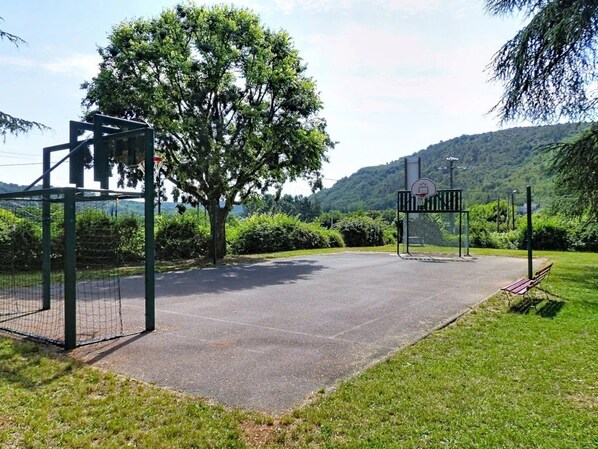 Un espacio pavimentado con un aro de baloncesto, un banco y un árbol.
