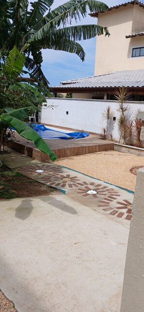 A patio area with a pool, a covered seating area, and a white wall.