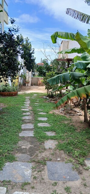 A garden pathway leading to a building with a white facade, surrounded by greenery and a clear sky.