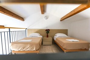 Une chambre avec deux lits, une table de chevet, un vase avec des fleurs et une rambarde de balcon.