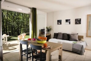 A room with a bed, a dining table with chairs, a small kitchen area, and a sliding glass door leading to an outdoor area.
