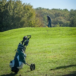 Un campo de golf con un bolso de golf en primer plano y un golfista a lo lejos.