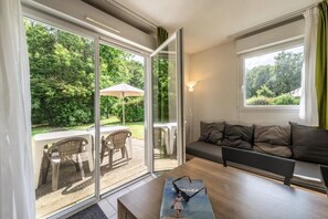 A room with a sofa, a table, and a view of a garden through large glass doors.