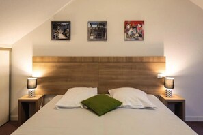 A bedroom with a wooden headboard, two bedside lamps, a bed with white and green pillows, and three framed pictures on the wall.