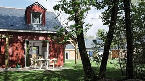 A red barn with a sloped roof, a small porch with chairs, and a grassy yard.