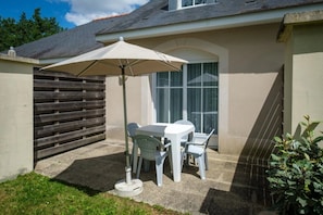 A patio with a table and chairs under a large umbrella, a wooden fence, and a window with curtains.
