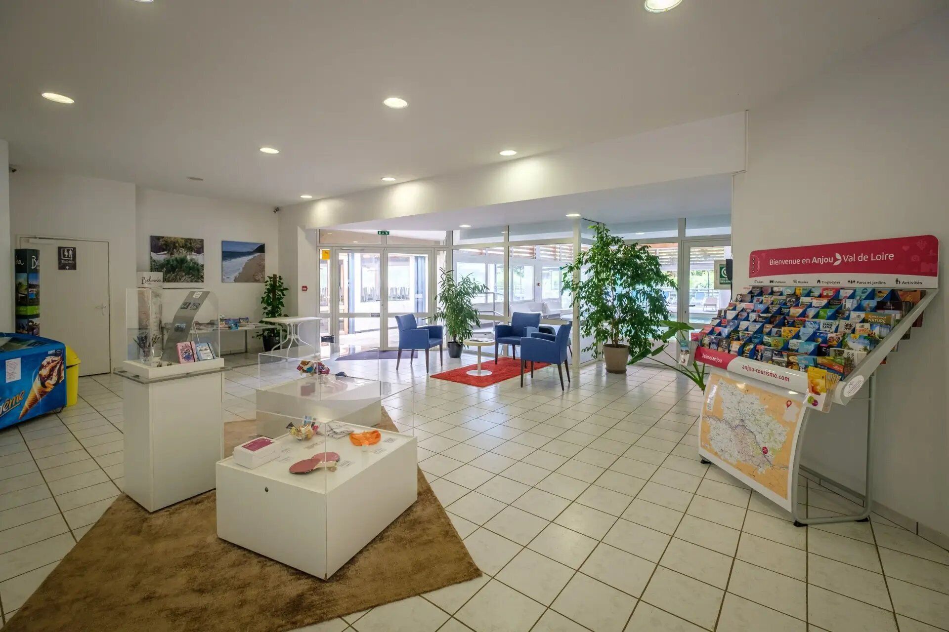 Een receptie met een wit receptiebalie, blauwe stoelen, een rood tapijt en een presentatie van reisbrochures.