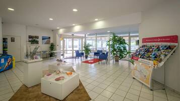 Een receptie met een wit receptiebalie, blauwe stoelen, een rood tapijt en een presentatie van reisbrochures.
