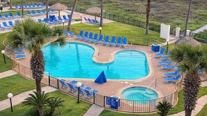 A pool area with multiple blue lounge chairs and palm trees. - Resort-like Beachfront - Heated Pool (South Padre Island)