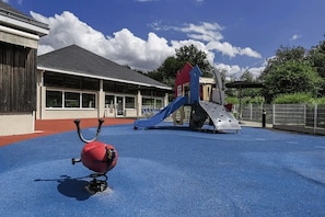 A playground with a slide and climbing structures, a red ball, and a building with large windows in the background.