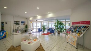 A reception area with a white reception desk, blue chairs, a red rug, and a display of travel brochures. - ZEcamping 3 étoiles piscine couverte pet friendly locatif TV LV BBQ (Saumur)