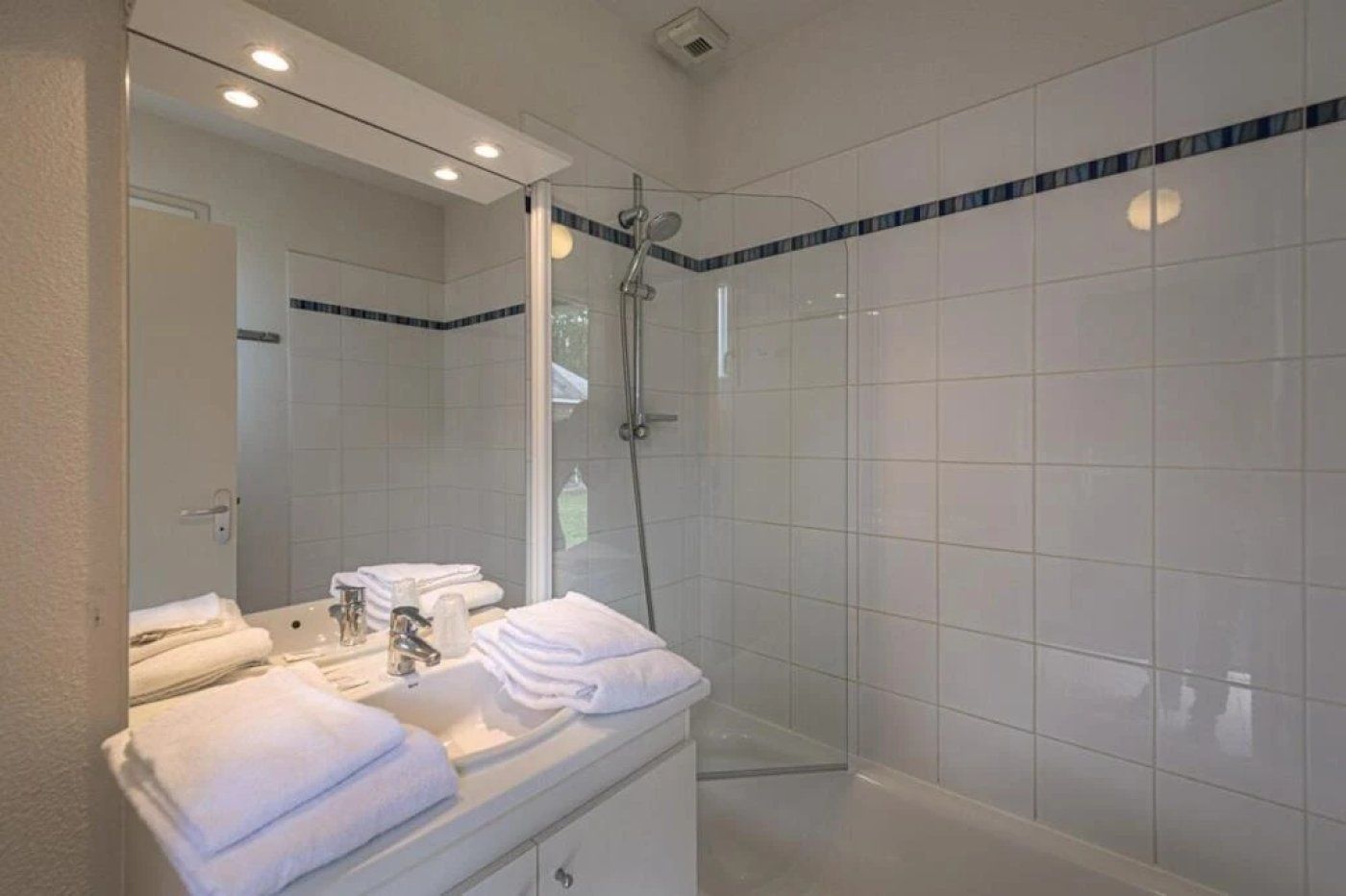 Une salle de bain moderne avec une douche à parois de verre, un meuble-lavabo avec un miroir et des serviettes soigneusement pliées.