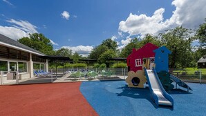 A playground with a slide and climbing structures, surrounded by a fenced area with lounge chairs. - ZEcamping 3 étoiles piscine couverte pet friendly locatif TV LV BBQ (Saumur)