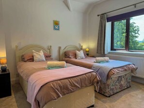 Une chambre avec deux lits, une fenêtre avec des rideaux, un radiateur et un petit élément de décoration murale.