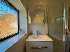 Une salle de bain dotée d’une grande fenêtre, d’un lavabo avec un miroir au-dessus et d’un espace douche.