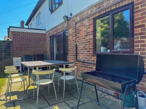 Une terrasse extérieure avec une table et des chaises, un barbecue et un mur en briques.