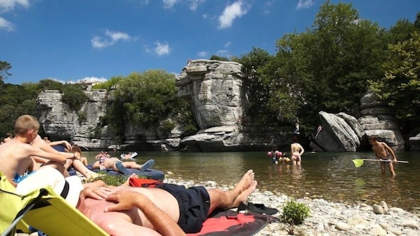 Une rive où des gens se détendent et se baignent, entourée de falaises rocheuses et de verdure.