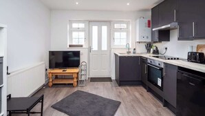 A modern kitchen with dark cabinets, a built-in oven, and a microwave. There is a wooden table with a TV and a small rug on the floor. - Relaxing Annexe | With Garden Access & Parking (Kent)