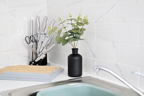 Un plan de travail de cuisine avec un vase noir contenant des plantes vertes, une planche à découper et un ensemble de couteaux.